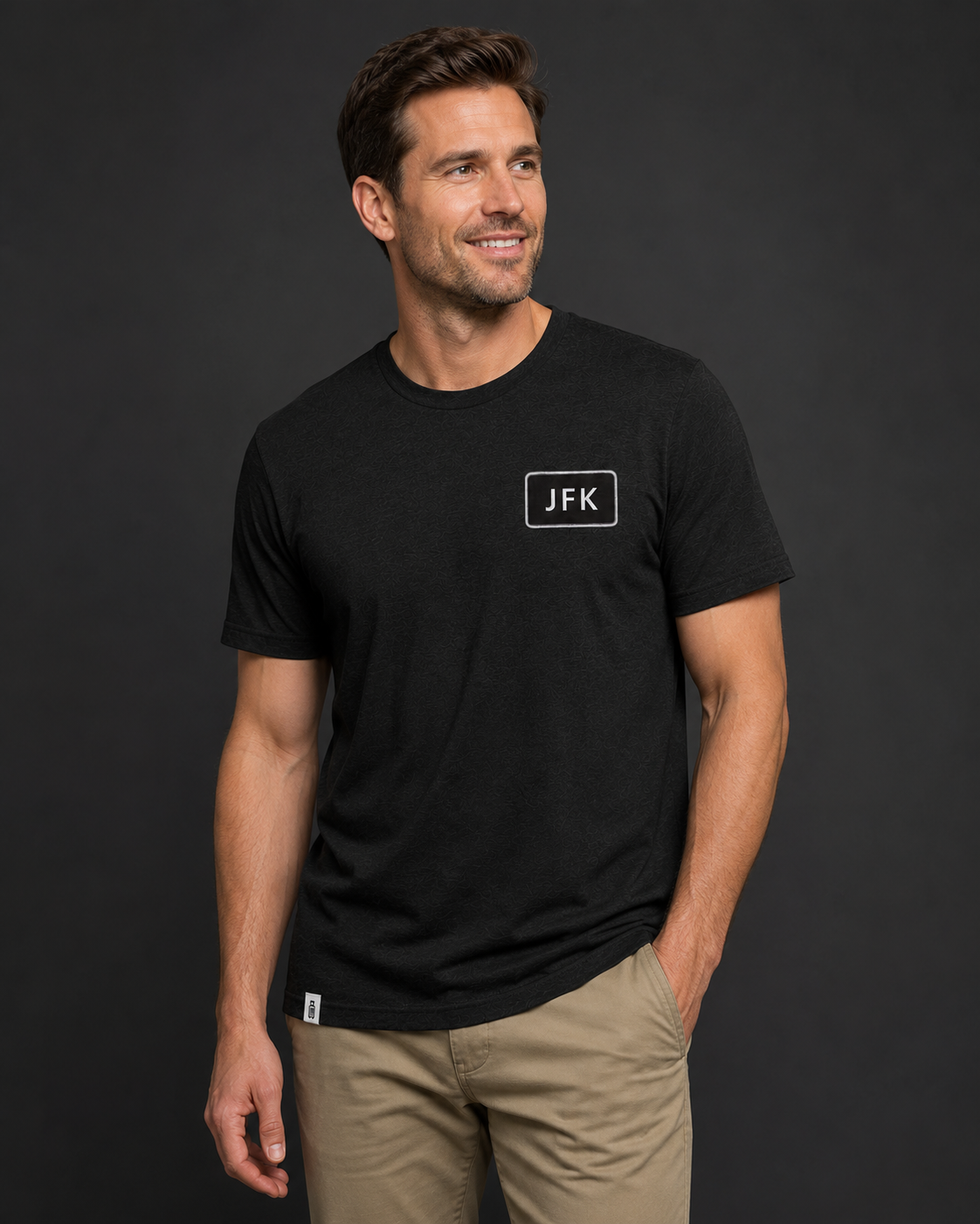 Man wearing a black t-shirt with 'JFK' logo against a dark background